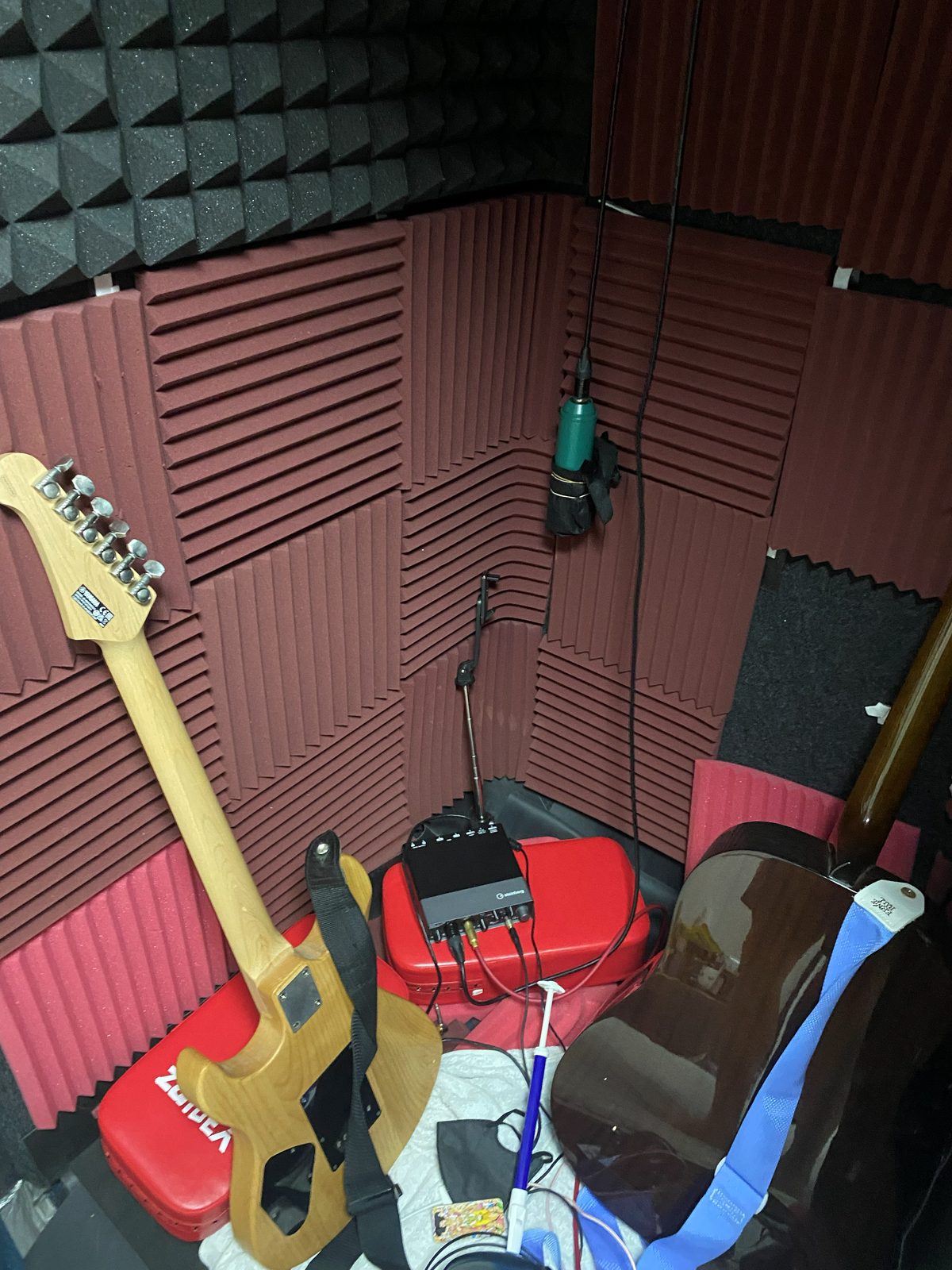 Indoor recording space with sound-absorbing material on the walls, an audio interface, a microphone, an electric guitar and an acoustic guitar